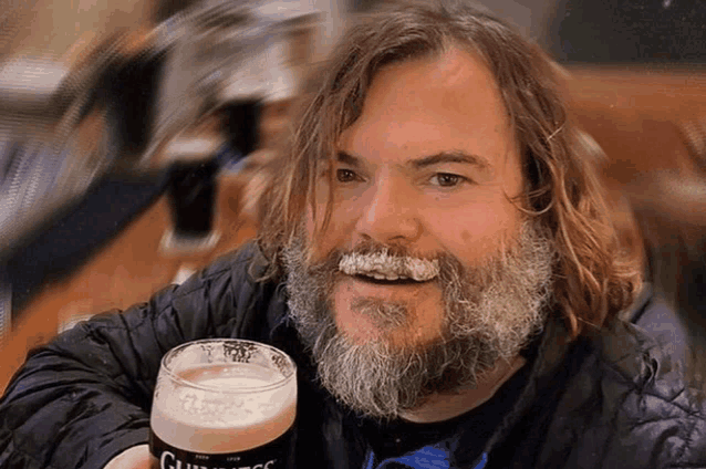 a man with a beard holds up a glass of guinness