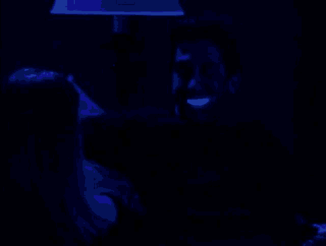 a man and a woman are sitting under a lamp in a dark room . the man is glowing in the dark .