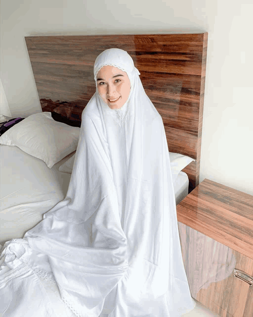 a woman wearing a white hijab sits on a bed