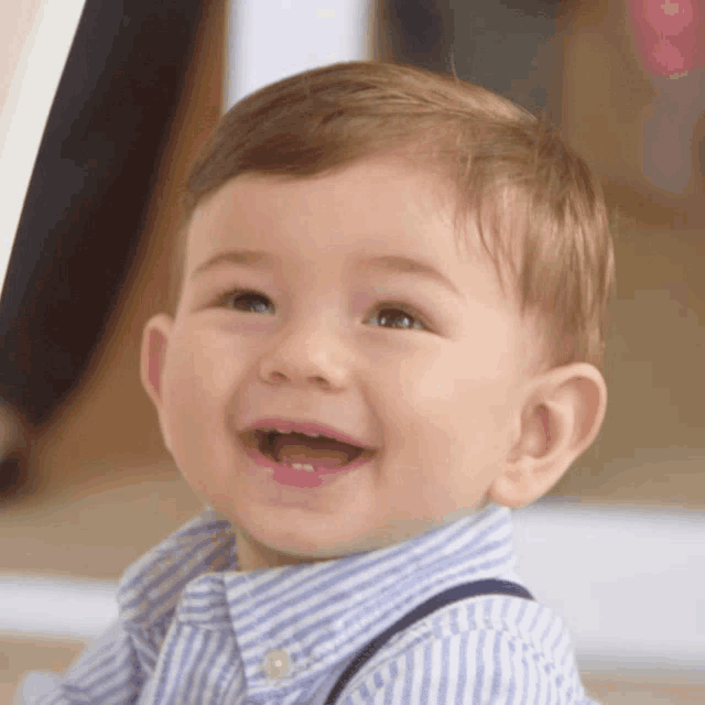 a baby boy wearing a striped shirt and suspenders is smiling