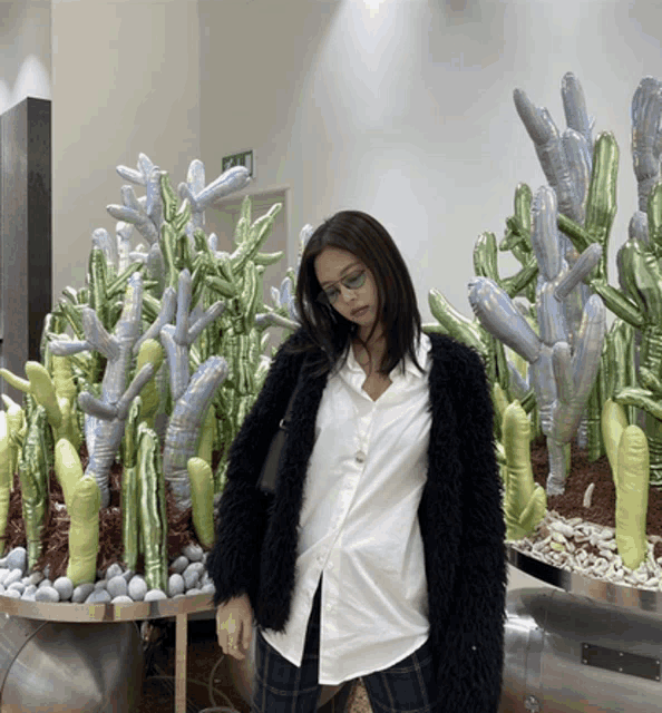 a woman in a white shirt and black jacket stands in front of a display of balloon cactus