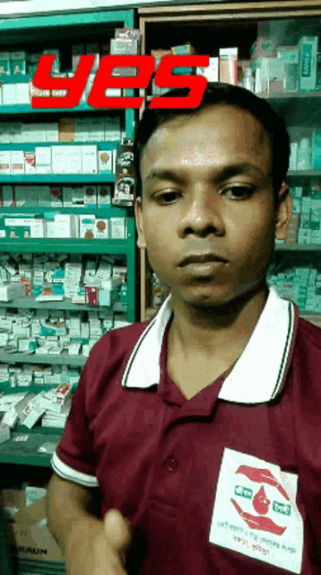 a man in a maroon shirt stands in front of a shelf full of medicines with the word yes above his head