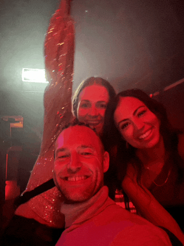 a man and two women pose for a picture in front of a red light