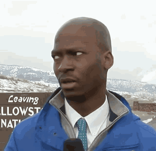 a man wearing a blue jacket and tie stands in front of a sign that says leaving yellowstone national park