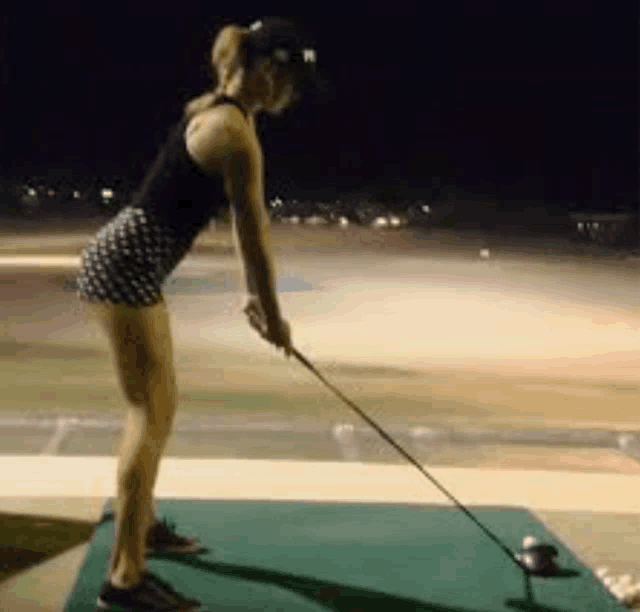 a woman is swinging a golf club at a golf ball on a golf course .