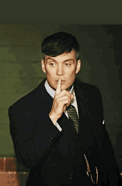 a man in a suit holds his finger to his lips