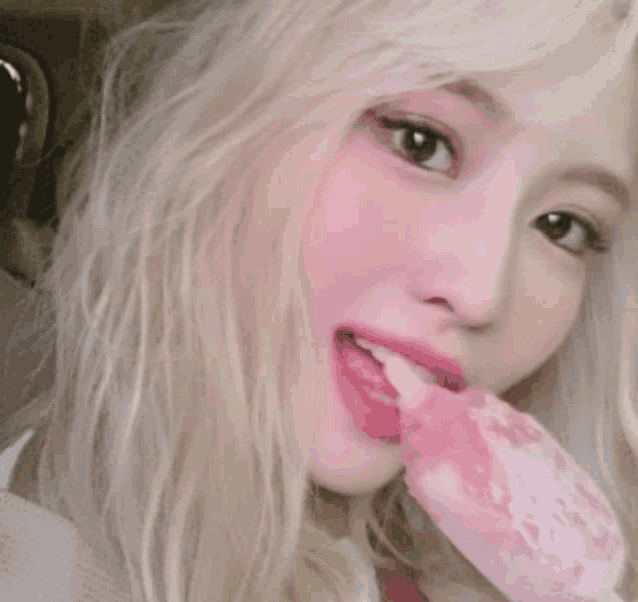 a blonde woman is eating a pink ice cream bar .