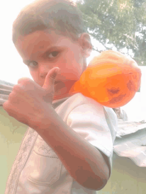 a young boy is holding an orange balloon and giving a thumbs up sign