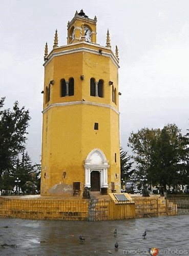 a yellow building with a clock on top of it and the words mexico enfotos on the bottom