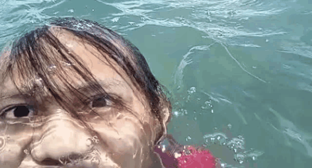 a little girl is swimming in the ocean and taking a selfie .