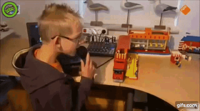 a man is talking into a microphone while sitting at a desk with a toy fire truck on it .