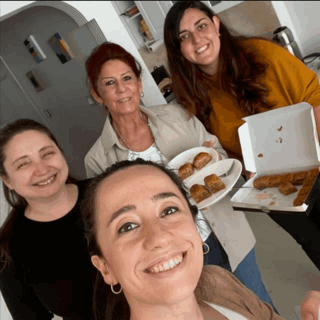 a group of women are posing for a picture and one of them is holding a box of food