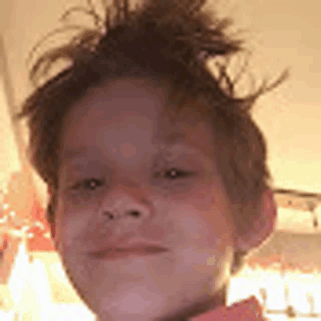 a young boy with messy hair is looking at the camera and smiling .