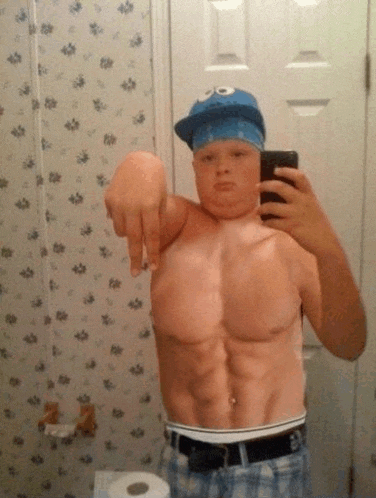 a shirtless man wearing a cookie monster hat takes a selfie in a bathroom