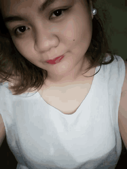 a woman wearing a white tank top and red lipstick is taking a selfie