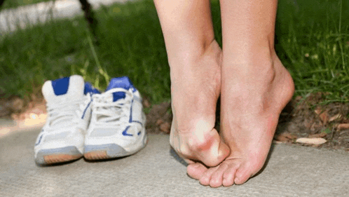 a woman 's bare feet are standing next to a pair of white and blue tennis shoes .