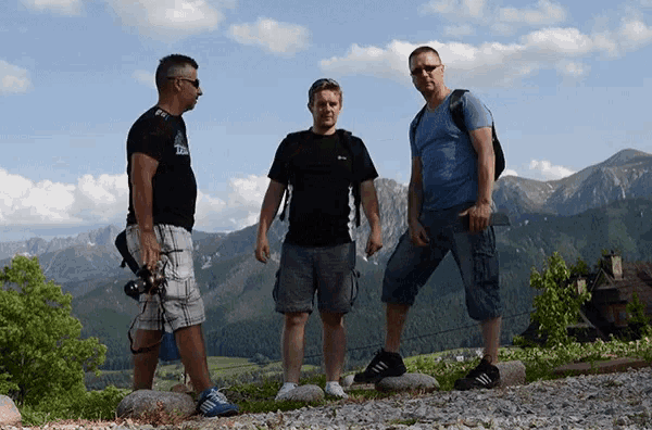 three men standing in front of a mountain with one wearing a t-shirt that says ' t-shirt ' on it