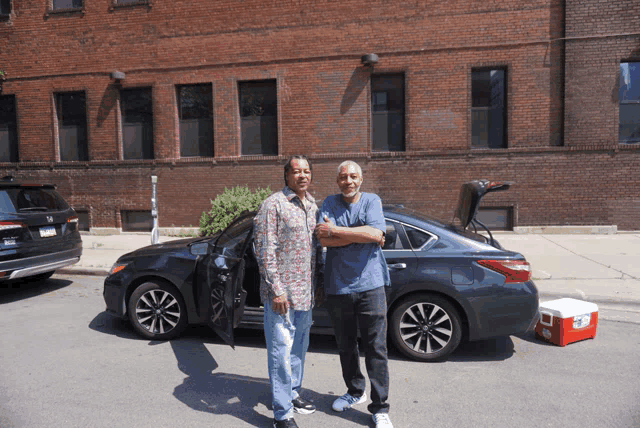 two men are standing in front of a car with a cooler in the back