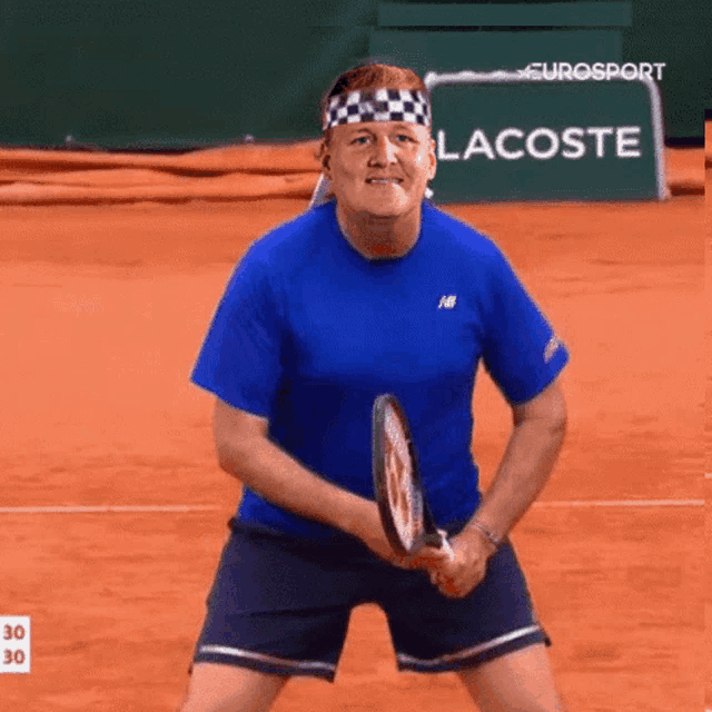 a man in a blue shirt is holding a tennis racket in front of a lacoste sign