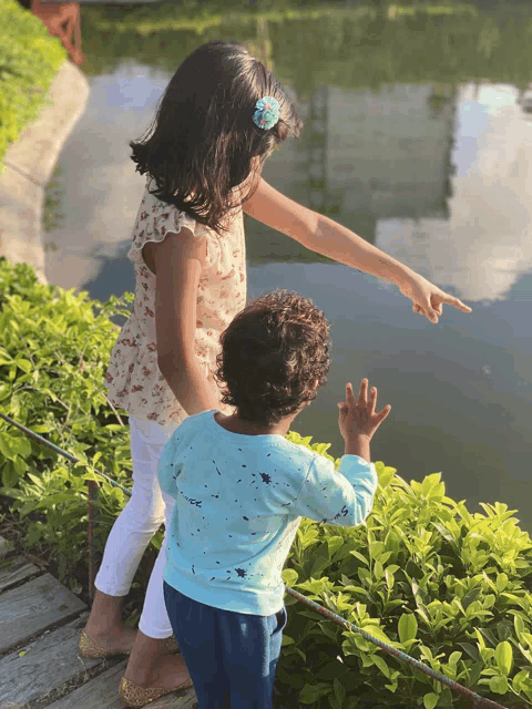 a little girl pointing at something in the water while a boy looks on