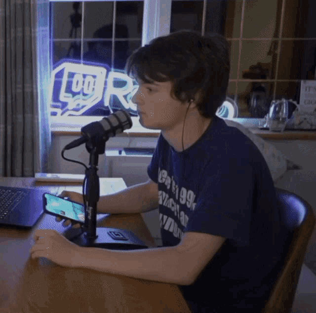 a man wearing a blue shirt that says ' chicago ' on it sits at a desk in front of a microphone