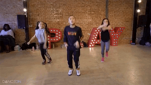 a group of young girls are dancing in front of a brick wall and a sign that says " play "