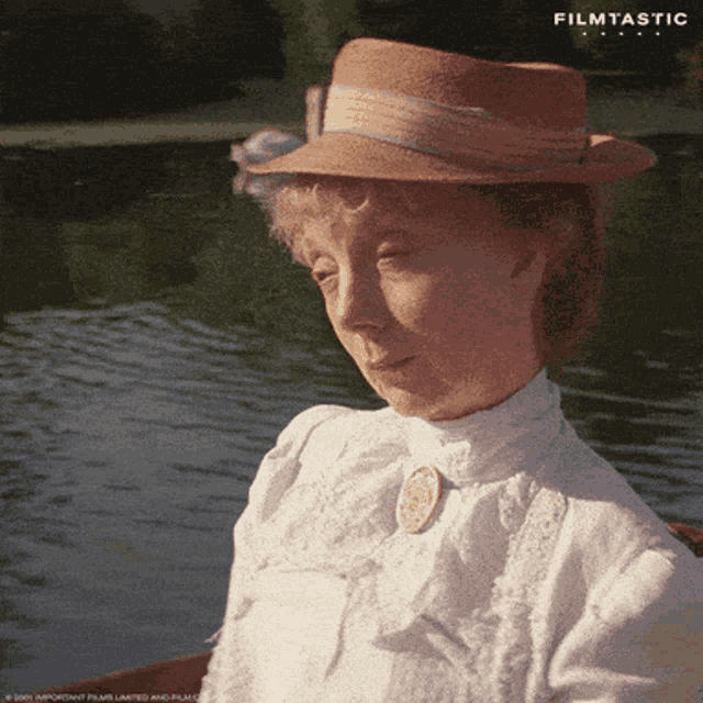 a woman wearing a straw hat and a white shirt is sitting in a boat in front of a lake