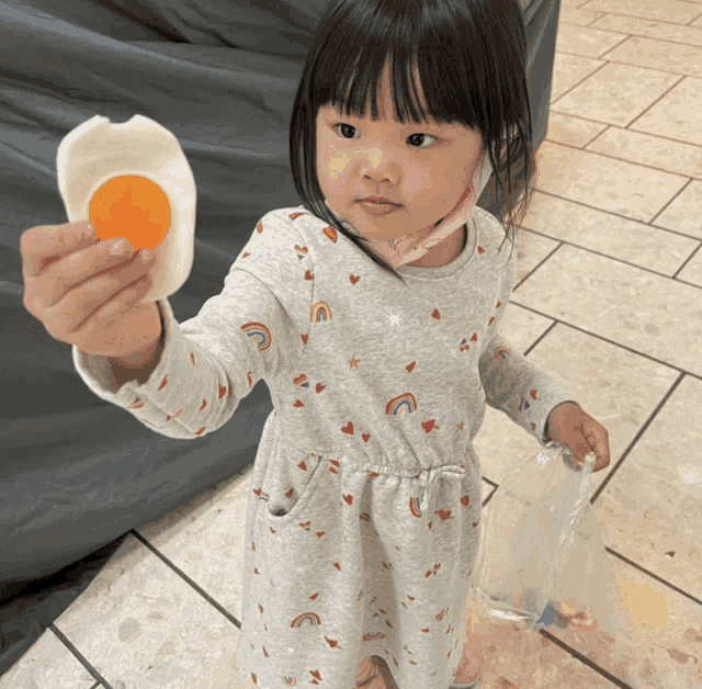 a little girl in a gray dress holds a fake egg