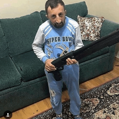 a man in a blue shirt is holding a shotgun in a living room .