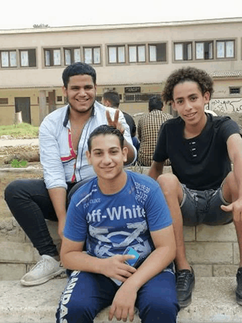 three young men are posing for a picture while sitting on a ledge .