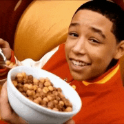 a young boy in a red jacket is holding a bowl of cereal and smiling