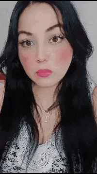 a woman with long black hair and pink lipstick is wearing a necklace and a white top .