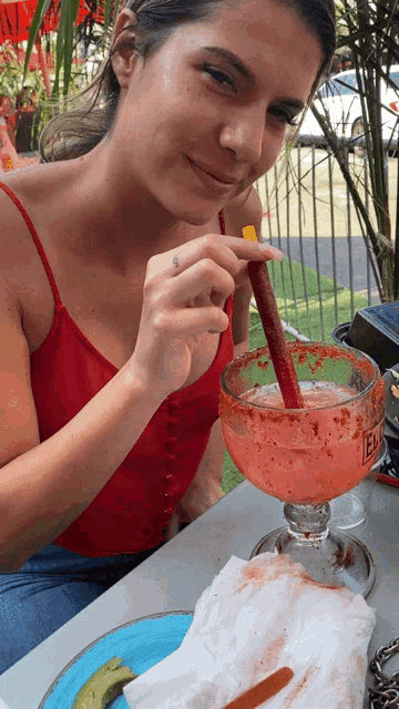 a woman in a red tank top is holding a straw in a margarita with the word el on the glass