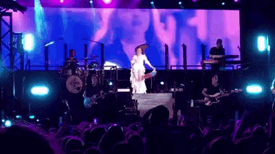 a woman in a white dress is playing a guitar on stage in front of a large screen that says youth