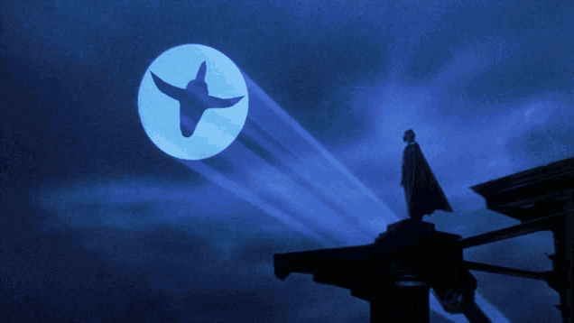 a man in a cape stands on top of a building in front of a blue moon with a bird on it