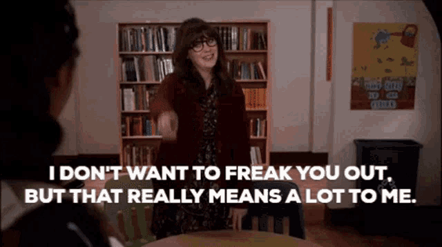 a woman is sitting at a table in front of a bookshelf and talking to another woman in a library .