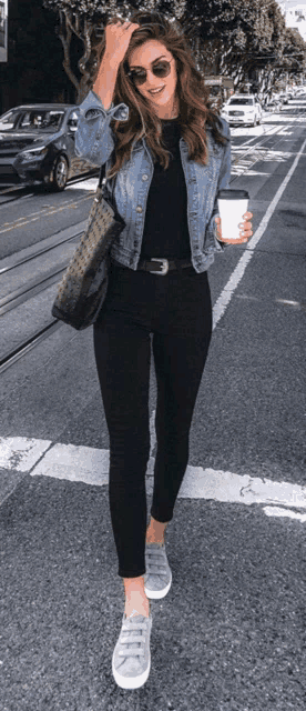 a woman wearing a denim jacket and black pants is walking down the street .