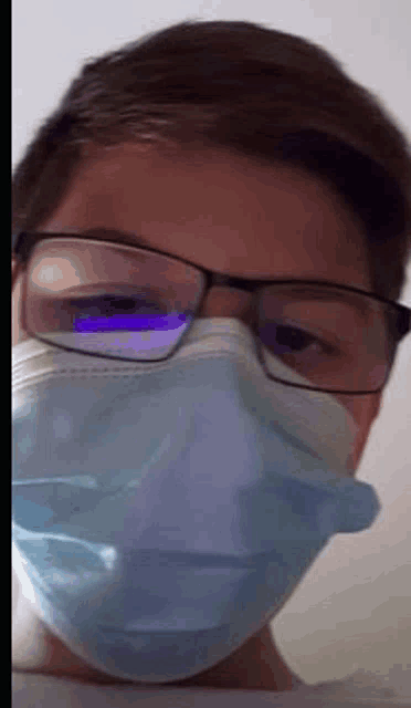 a young man wearing glasses and a face mask is looking at the camera .