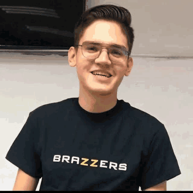 a young man wearing glasses and a black brazzers t-shirt is smiling .