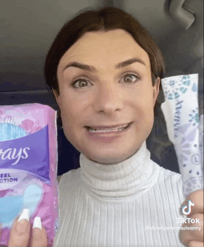 a woman in a white sweater is holding a pack of pads and a tube of wipes