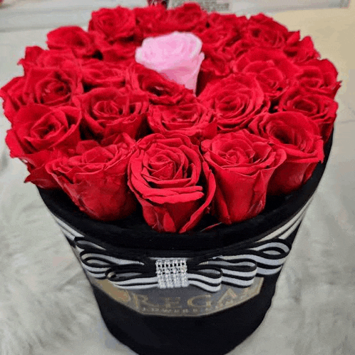 a black box filled with red roses and a pink rose in the middle