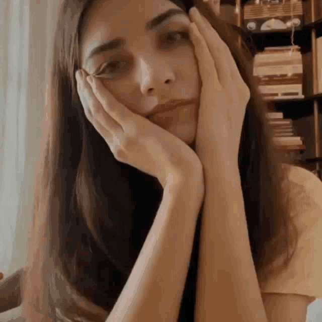 a woman rests her head on her hands in front of a book shelf