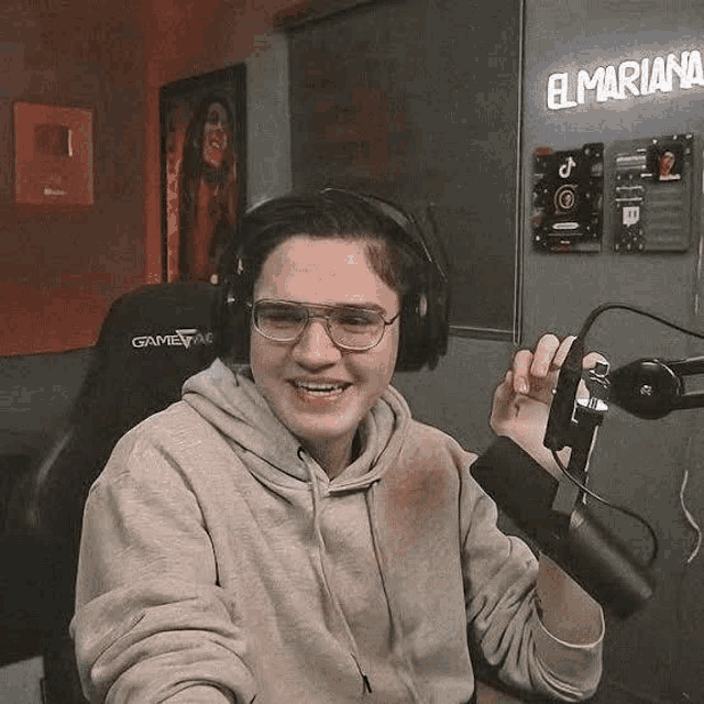 a man wearing headphones and glasses is sitting in front of a microphone and smiling .