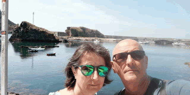 a man and a woman wearing sunglasses pose for a photo in front of a body of water