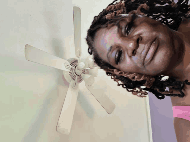 a woman with dreadlocks looks down at a ceiling fan