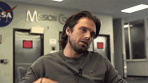 a man with long hair and a beard is sitting at a table in front of a nasa sign .