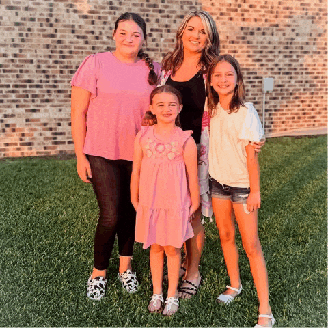 a woman and three little girls pose for a picture in front of a brick wall