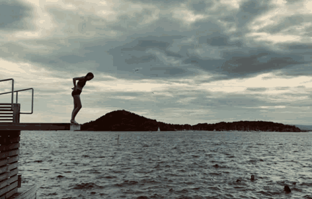 a woman stands on a diving board overlooking the water