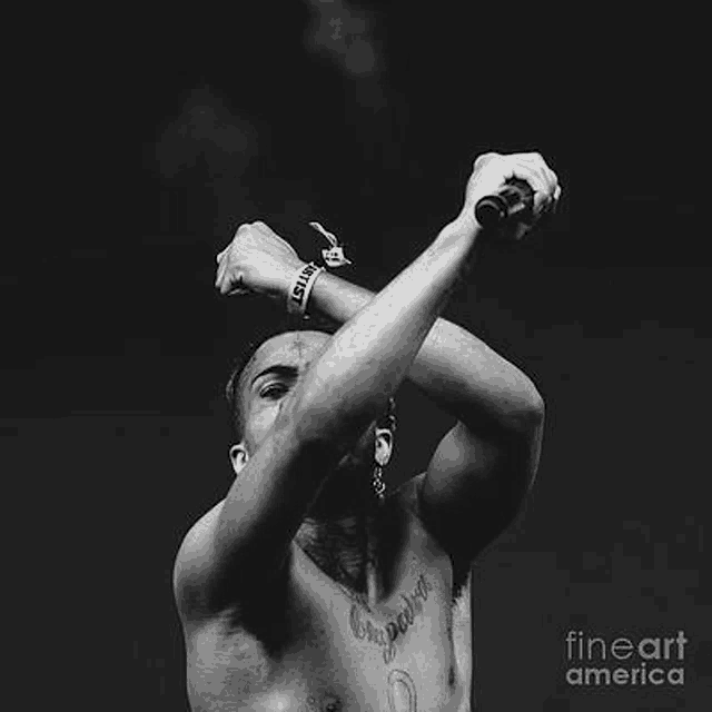 a black and white photo of a shirtless man singing into a microphone on a stage .