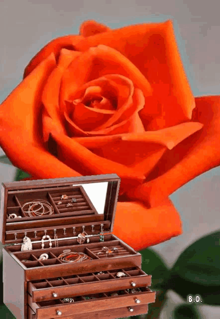 an orange rose is behind a wooden jewelry box with drawers